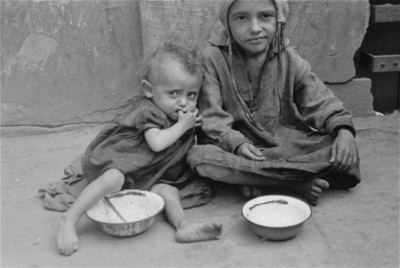 Two children begging on a sidewalk in the Warsaw ghetto. - Ghetto, Children, Hunger